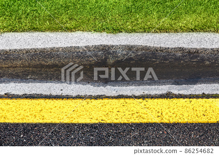 puddle on drain canal near asphalt road with stormwater on the road side with ditch for water after rain and glade of green lawn along highway with yellow marking. 86254682