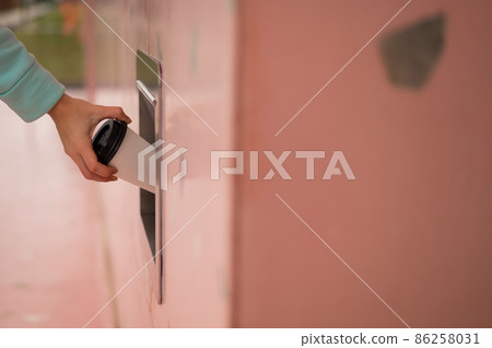 A woman throws a cup of coffee into a garbage manhole in the wall of a cafe. 86258031