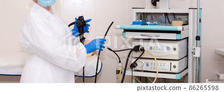 Doctor gastroenterologist in protective clothing holding endoscope before gastroscopy. Medical examination, medicine utensils and instruments, gastrointestinal fiberoptic endoscopy at modern hospital. Doctor gastroenterologist in protective clothing holding endoscope before gastroscopy. Medical examination, medicine utensils and instruments, gastrointestinal fiberoptic endoscopy at modern hospital. 86265598