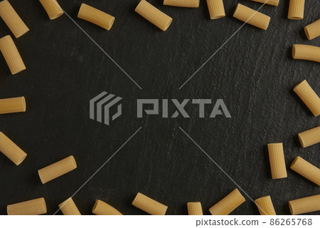 pasta concept some of the large, tube-shaped rigatoni pasta with ridged edges being organized in a circle on the black background 86265768