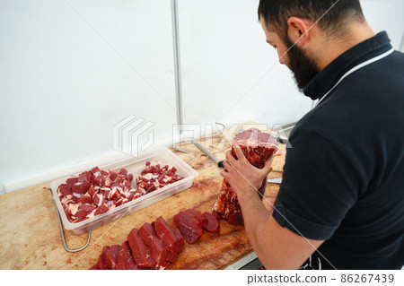 Butcher cutting slices of raw meat on wooden board Butcher cutting slices of raw meat on wooden board 86267439