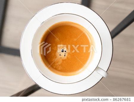 Espresso coffee in a white cup stands on a glass table Espresso coffee in a white cup stands on a glass table 86267681
