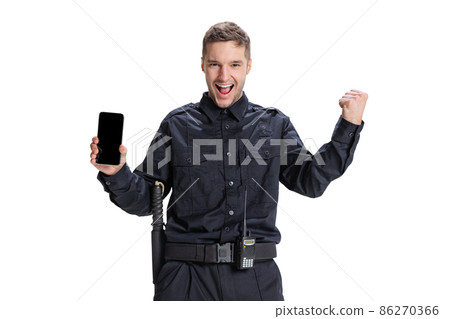 Portrait of young man, policeman officer wearing black uniform using phone isolated on white background. Concept of job, caree, law and order. Portrait of young man, policeman officer wearing black uniform using phone isolated on white background. Concept of job, caree, law and order. 86270366