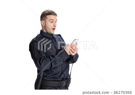 Shocked young man, policeman officer wearing black uniform using phone isolated on white background. Concept of job, caree, law and order. Shocked young man, policeman officer wearing black uniform using phone isolated on white background. Concept of job, caree, law and order. 86270368