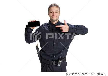 Portrait of young man, policeman officer wearing black uniform using phone isolated on white background. Concept of job, caree, law and order. Portrait of young man, policeman officer wearing black uniform using phone isolated on white background. Concept of job, caree, law and order. 86270375