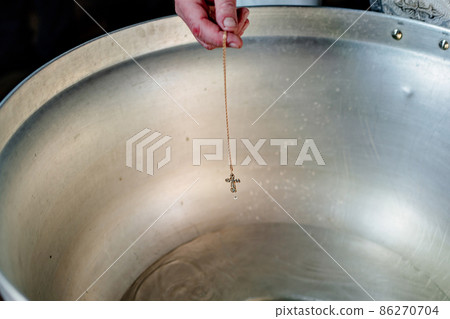 a cross on a gold chain is dipped in water for baptism in the font of the church.  86270704