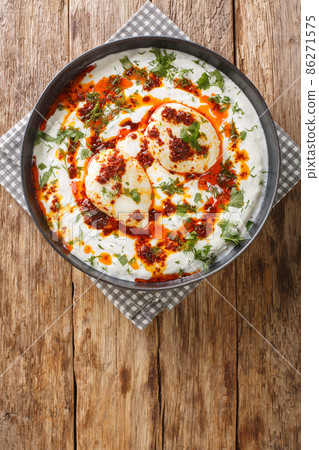 Cilbir is a Turkish egg dish reminiscent of a poached egg. prepared with yoghurt, garlic served with melted butter soaked in Aleppo pepper closeup in the plate. Vertical top view 86271575