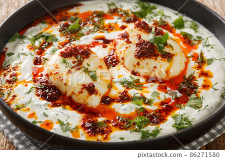 Turkish simple savory breakfast Cilbir is perfectly poached eggs, served over a delicious garlicky yogurt and spicy butter with red pepper flakes closeup in the plate. Horizontal Turkish simple savory breakfast Cilbir is perfectly poached eggs, served over a delicious garlicky yogurt and spicy butter with red pepper flakes closeup in the plate. Horizontal 86271580