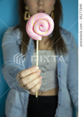 Happy beautiful woman giving colorful pink twirl lollipop on light blue background. Sweets,hard candy,gift,present concept 86271946
