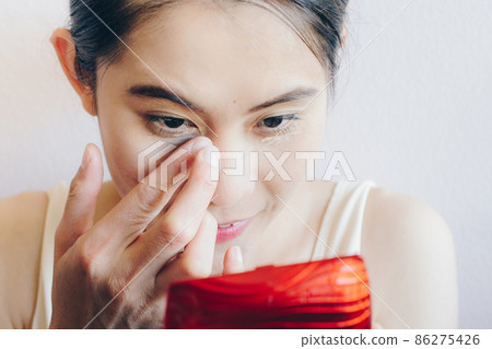 Close up shot of Asian woman face marking and applying cream concealer on her under eyes. Concealer is a type of cosmetic that is used to mask dark circles, age spots, large pores etc. Close up shot of Asian woman face marking and applying cream concealer on her under eyes. Concealer is a type of cosmetic that is used to mask dark circles, age spots, large pores etc. 86275426