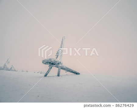 Minimalistic winter background with a frozen wooden chair with a frosty haze against the pink sky of the polar day. Minimalistic winter background with a frozen wooden chair with a frosty haze against the pink sky of the polar day. 86276429