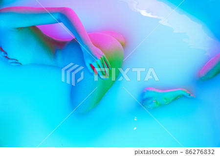 Top view of slim young girl lying in the milk bath with soft pink neon glow. Beauty, fashion, style, bodycare, spa concept. Top view of slim young girl lying in the milk bath with soft pink neon glow. Beauty, fashion, style, bodycare, spa concept. 86276832