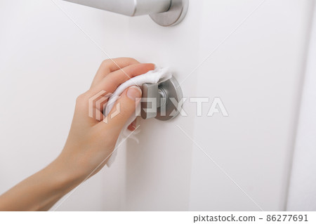 Cleaning door handles with an antiseptic wet wipe and gloves. Sanitize surfaces prevention in hospital and public spaces against corona virus. Woman hand using towel for cleaning home room door link. Cleaning door handles with an antiseptic wet wipe and gloves. Sanitize surfaces prevention in hospital and public spaces against corona virus. Woman hand using towel for cleaning home room door link. 86277691