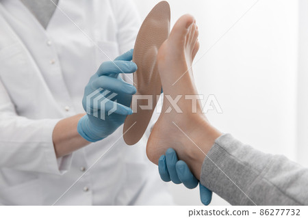 Doctor hands hold an orthopedic insole. Orthopedist tests the medical device. Orthopedic insoles on a white background. Foot care, comfort for the feet. Prevention of flat feet and foot diseases. Doctor hands hold an orthopedic insole. Orthopedist tests the medical device. Orthopedic insoles on a white background. Foot care, comfort for the feet. Prevention of flat feet and foot diseases. 86277732