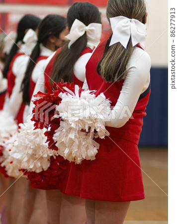 Cheerleaders standing with their pom poms behind them at a basketball game Cheerleaders standing with their pom poms behind them at a basketball game 86277913