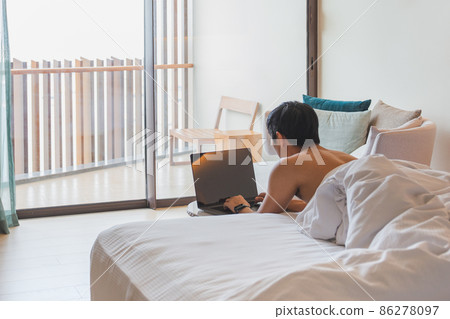 Man working on laptop lying in bed on vacation. 86278097