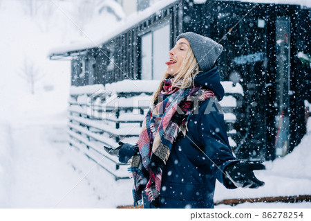 A young woman sticks out her tongue to catch snowflakes during a snow storm. A young woman sticks out her tongue to catch snowflakes during a snow storm. 86278254