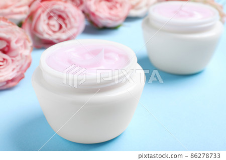 Open jars of cream and flowers on blue background, closeup Open jars of cream and flowers on blue background, closeup 86278733