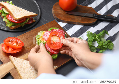 Woman adding tomato to sandwich at black table, closeup 86279085