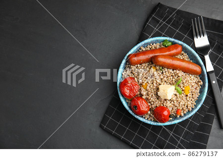 Tasty buckwheat porridge with sausages on dark grey table, flat lay. Space for text 86279137