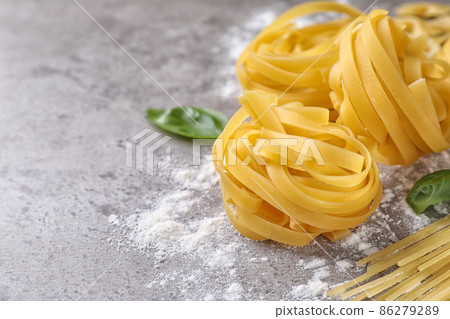 Uncooked tagliatelle pasta on grey table, closeup. Space for text 86279289