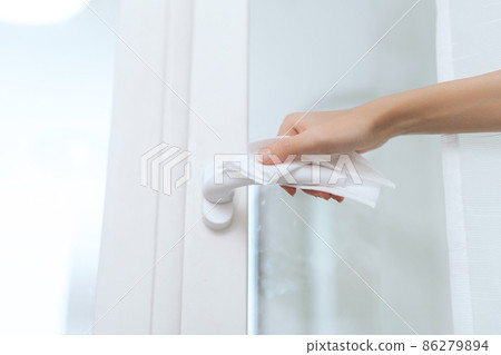 Cleaning door handles with an antiseptic wet wipe and gloves. Woman hand using towel for cleaning home room door link. Sanitize surfaces prevention in hospital and public spaces against corona virus. 86279894