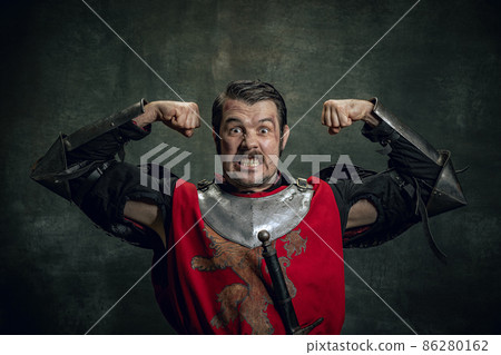 Portrait of brave medieval warrior or knight with dirty wounded face looking at camera isolated over dark background. Comparison of eras 86280162