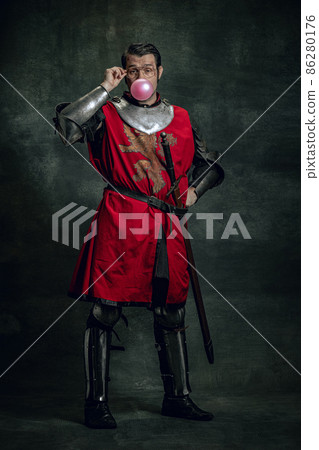 One cheerful medieval warrior or knight with dirty face in war equipment having fun isolated over dark background. Comparison of eras 86280176