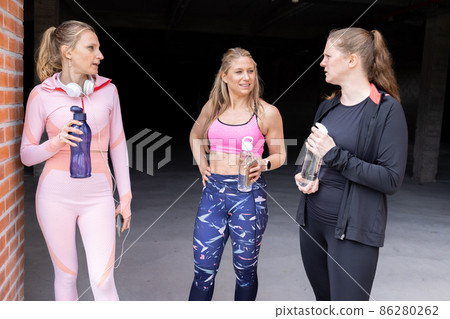 Sporty beautiful young women of different body types talking and drinking water from bottle after Sporty beautiful young women of different body types talking and drinking water from bottle after 86280262