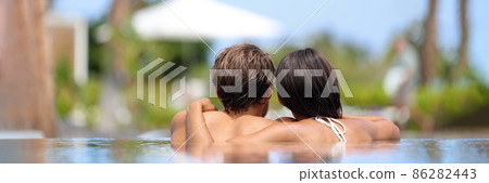 Luxury spa couple relaxing at pool resort hot tub panoramic view from behind of two people. Adults only hotel travel vacation getaway for honeymoon. Woman and man hugging. 86282443