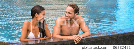 Swimming pool luxury vacation at resort. Happy hotel guests swimsuit models couple smiling on travel holiday summer vacations. Asian woman, caucasian man lovers on honeymoon banner. Swimming pool luxury vacation at resort. Happy hotel guests swimsuit models couple smiling on travel holiday summer vacations. Asian woman, caucasian man lovers on honeymoon banner. 86282451