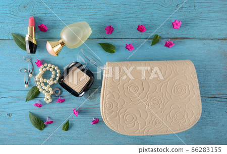 Elegant handbag,cosmetics powder, lipstick perfume, pearl necklace and earrings on a blue vintage background. 86283155