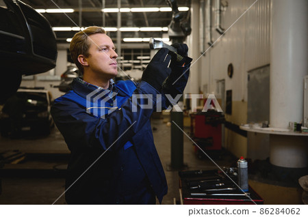 Technician, auto mechanic, car engineer working in repair shop or car service garage against a lifted car with open hood 86284062