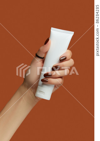 Womans hand holding white tube on brown background. Self care concept. Womans hand holding white tube on brown background. Self care concept. 86284285
