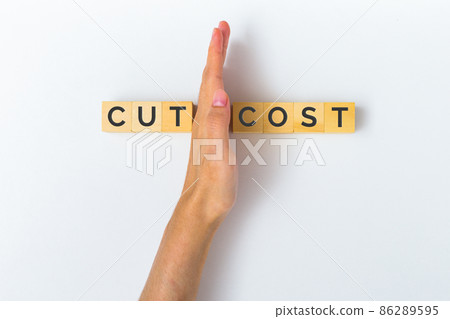 Hand cutting wooden block with text CUT COST, savings, business, recession, wasteful, commission, cash back, taxes, Concept of budget cuts. 86289595
