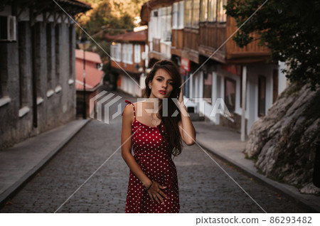Sexy young Caucasian girl in red dress posing on beautiful historical street in Europe Sexy young Caucasian girl in red dress posing on beautiful historical street in Europe 86293482