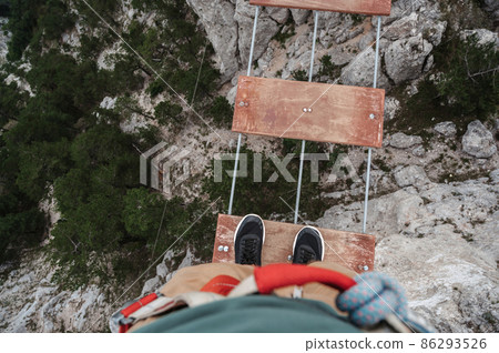 feet of male tourist crossing a abyss in mountains on a suspension bridge 86293526