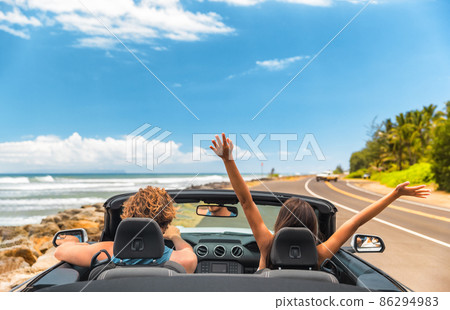 Road trip car holiday happy couple driving convertible car on summer travel Hawaii vacation. Woman with arms up having fun, young man driver. 86294983