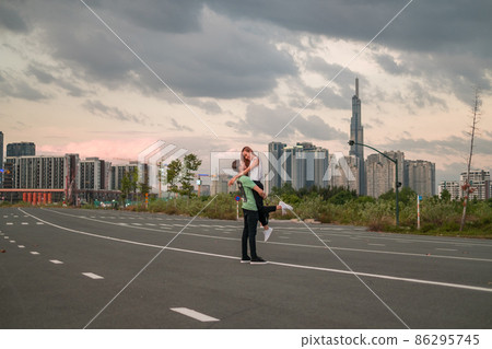 Lovely young couple walking on the street in the big city on the sunset. Boyfriend holding girlfriend in his arms. Skyscrapers on the background Lovely young couple walking on the street in the big city on the sunset. Boyfriend holding girlfriend in his arms. Skyscrapers on the background 86295745