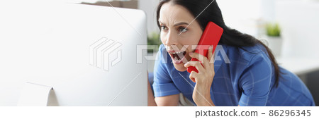 Young shocked woman talking on smartphone and looking at computer monitor 86296345