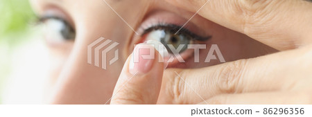 Woman puts on soft contact lens over eyes closeup Woman puts on soft contact lens over eyes closeup 86296356