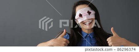 Smiling woman in mask on face holds thumbs up 86296374