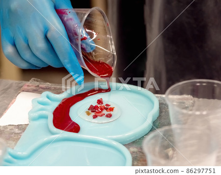 The art process of pouring epoxy resin into a wooden toy. Technology process of creating a painting in style resin art, works with epoxy in studio, makes a wooden stand with the image. Close up. 86297751