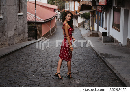Beautiful sexy brunette girl in a red dress posing on street with paving stones in Italy Beautiful sexy brunette girl in a red dress posing on street with paving stones in Italy 86298451