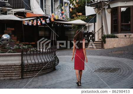 beautiful brunette girl in red dress walks along the cobblestones in beautiful old European town beautiful brunette girl in red dress walks along the cobblestones in beautiful old European town 86298453