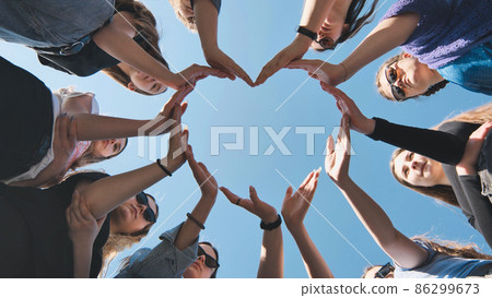 Cheerful girlfriends make a heart shape out of their hands. Cheerful girlfriends make a heart shape out of their hands. 86299673