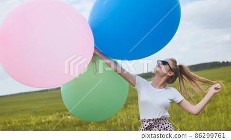 Happy girl with big multicolored balloons posing on the field. Happy girl with big multicolored balloons posing on the field. 86299761