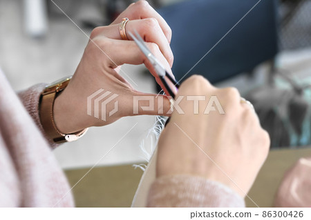 Female hands, white, 30-35 years old, cuts the seam with small scissors. Clothes repair in the studio, remodels. Concept: atelier, sewing courses, sewing hobbies. 86300426