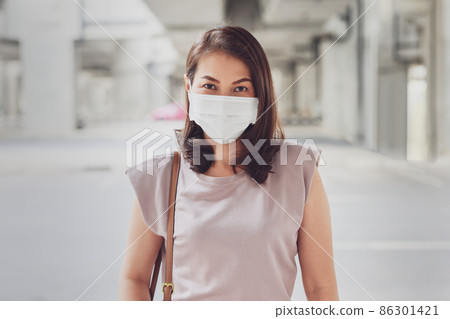 Asian woman wearing protective face mask standing and looking at camera outside in an urban construction background with copy space. Concept of new normal lifestyle and prevents the COVID-19 virus Asian woman wearing protective face mask standing and looking at camera outside in an urban construction background with copy space. Concept of new normal lifestyle and prevents the COVID-19 virus 86301421