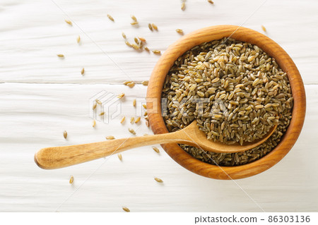 Organic Raw Cracked Wheat Freekah in a Bowl with wood spoon on rustic table. Horizontal top view 86303136